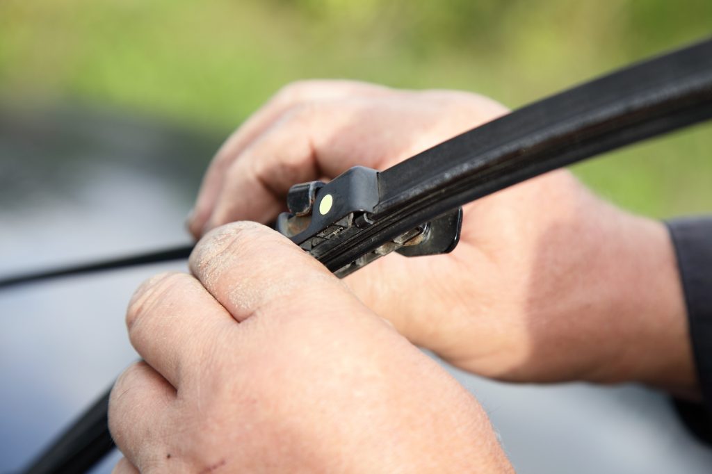 Replacement of car wiper blades, seasonal vehicle maintenance, male hands close-up on the background of green grass