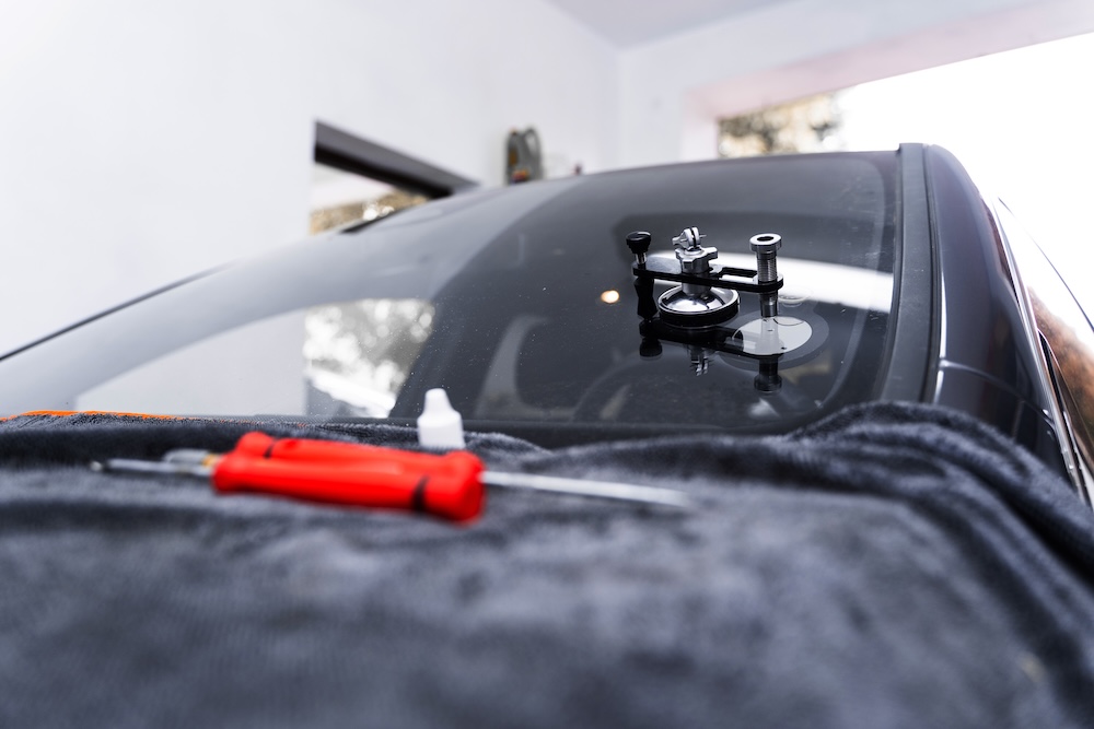 Resin repair on windshield using injector application to restore structural clarity. Windshield crack repair using resin injection. Technician using windshield injector tool to fix bullseye crack