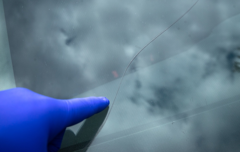 A crack on the windshield of the car.Replacement of auto glass. Elimination of cracks and chips on the car glass. A gloved hand points to a cracked car window.