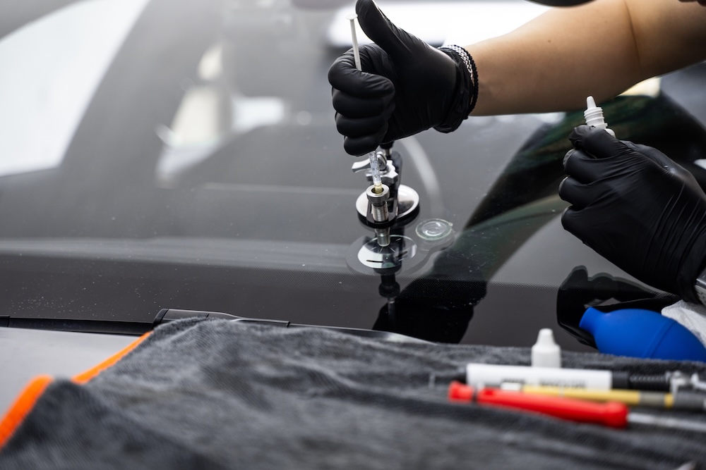 Windshield crack repair using resin injection. Technician using windshield injector tool to fix bullseye crack. Resin repair on windshield using injector application to restore structural clarity